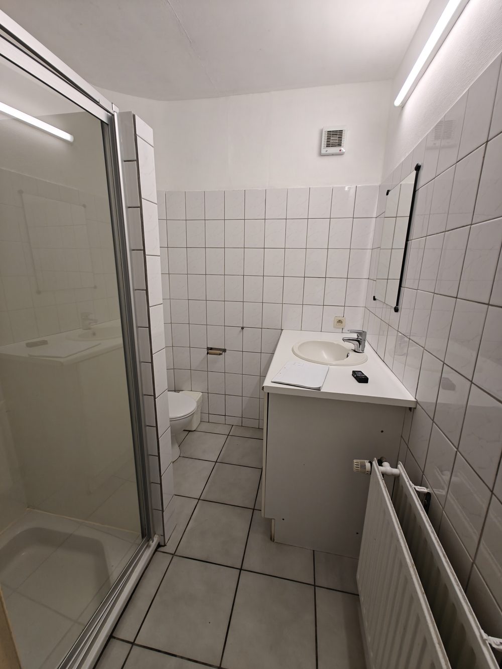 Avant travaux : salle de bain en carrelage blanc avec ancienne cabine de douche